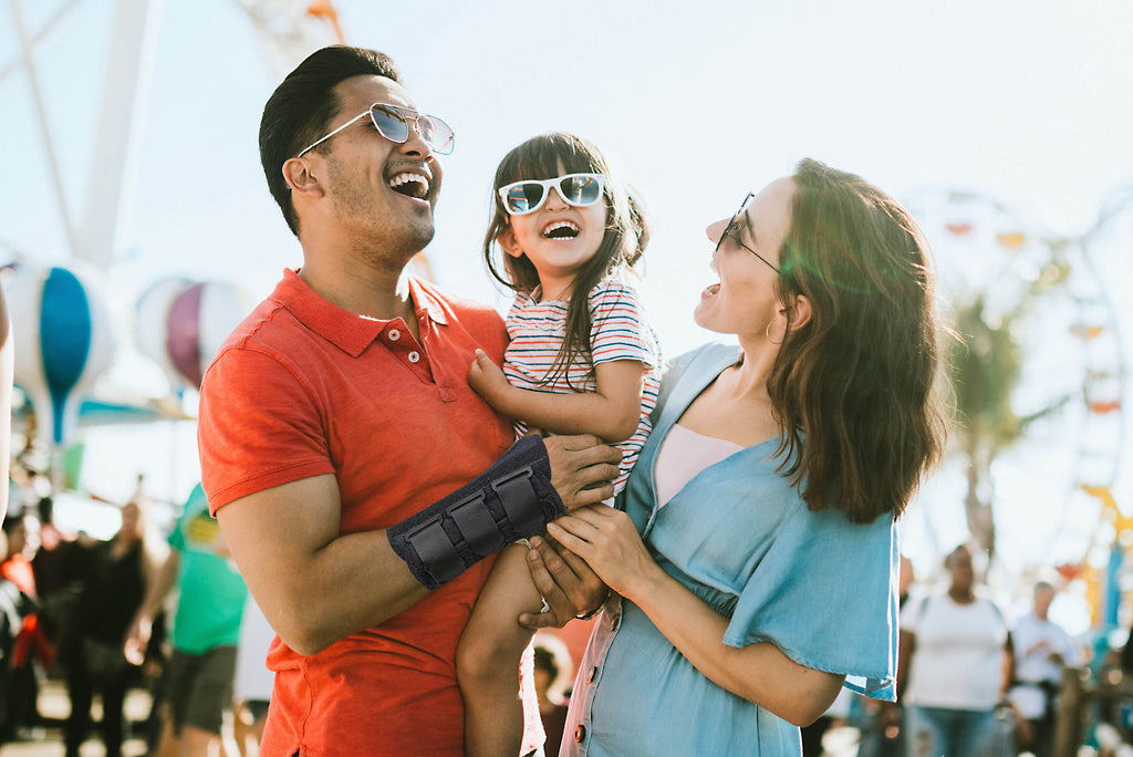 Image of a couple holding their baby at an amusement park on a hot summer day with the father's wrist wrapped with 1142 Universal Wrist Orthosis on right wrist