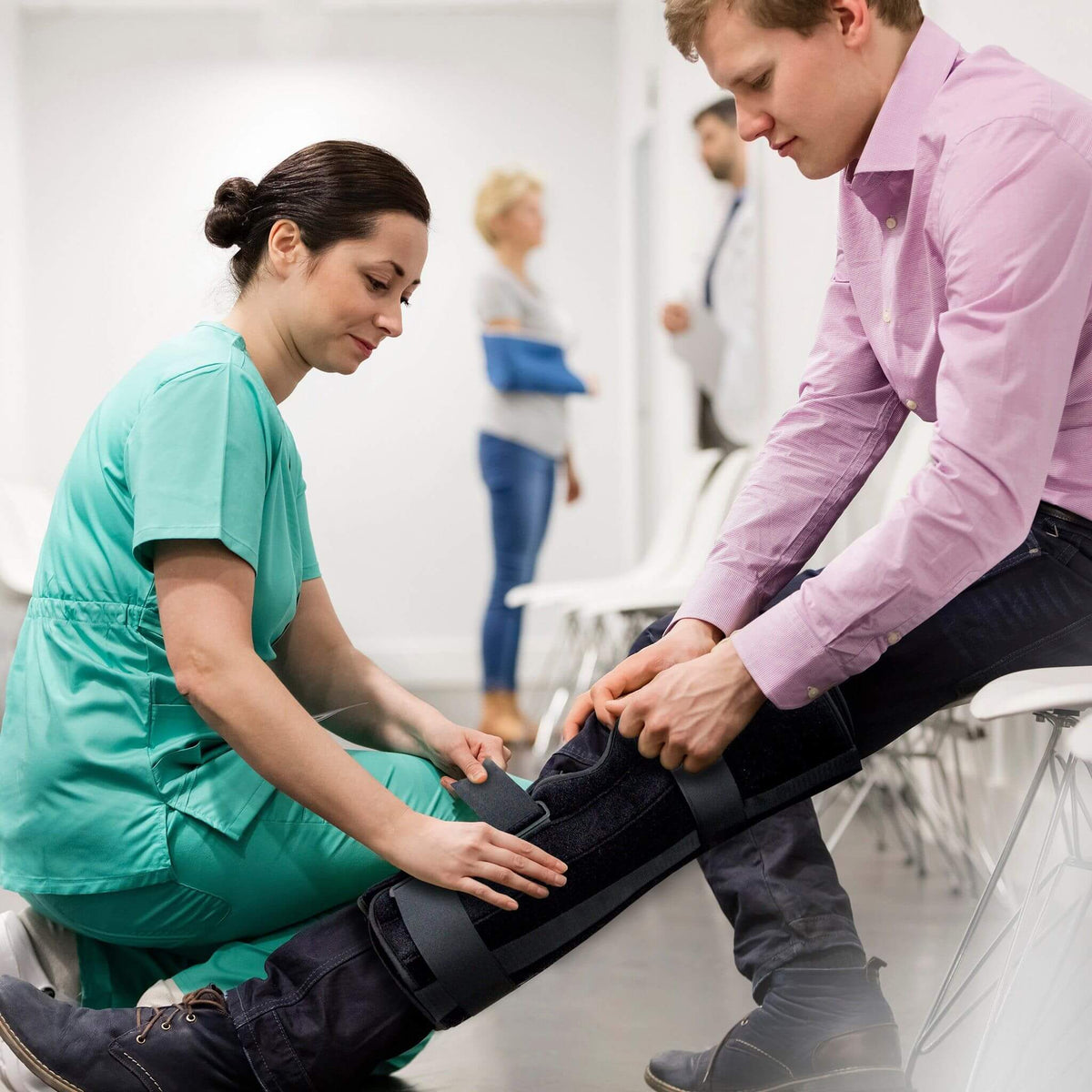 Medical professional fitting an EzyWrap Tri-Panel Knee Immobilizer on a patient during post-operative knee recovery and rehabilitation.